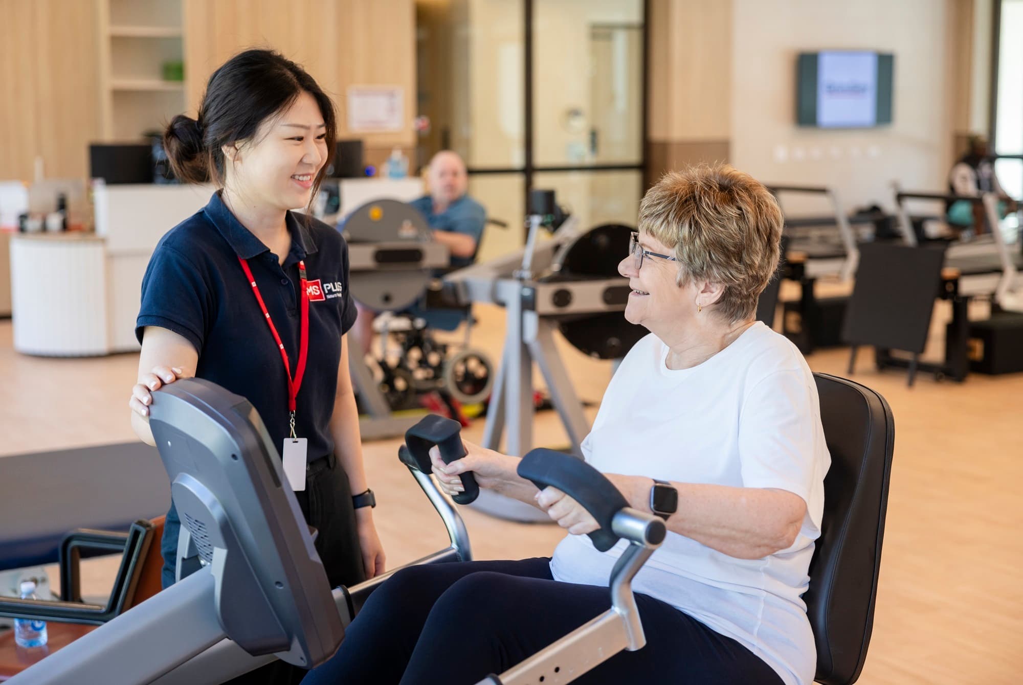 An MS Plus Allied Health worker with an MS Plus client doing exercise on a stationery machine.