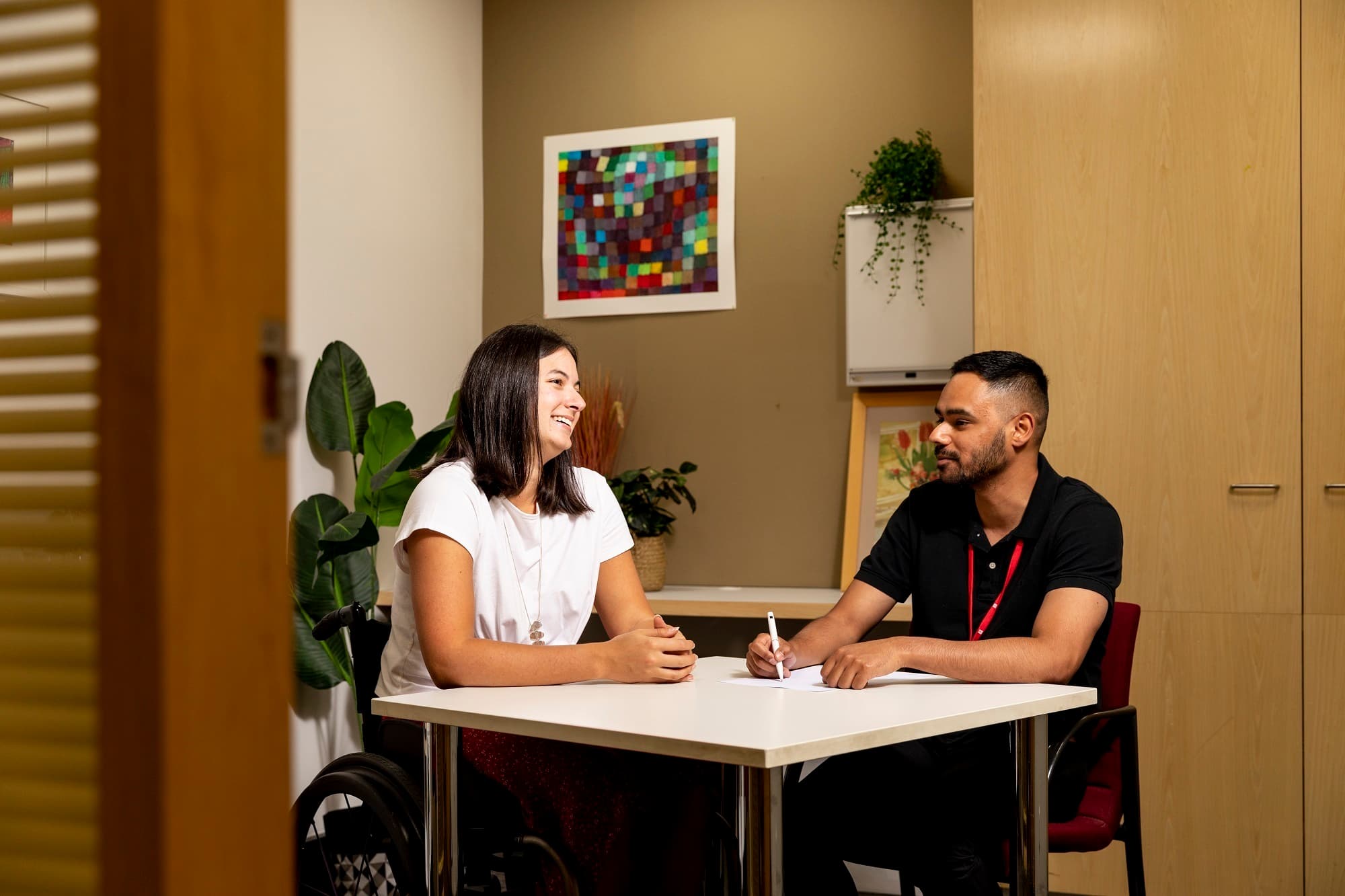 An MS Plus occupational therapist seated at table taking notes, with an MS Plus client.