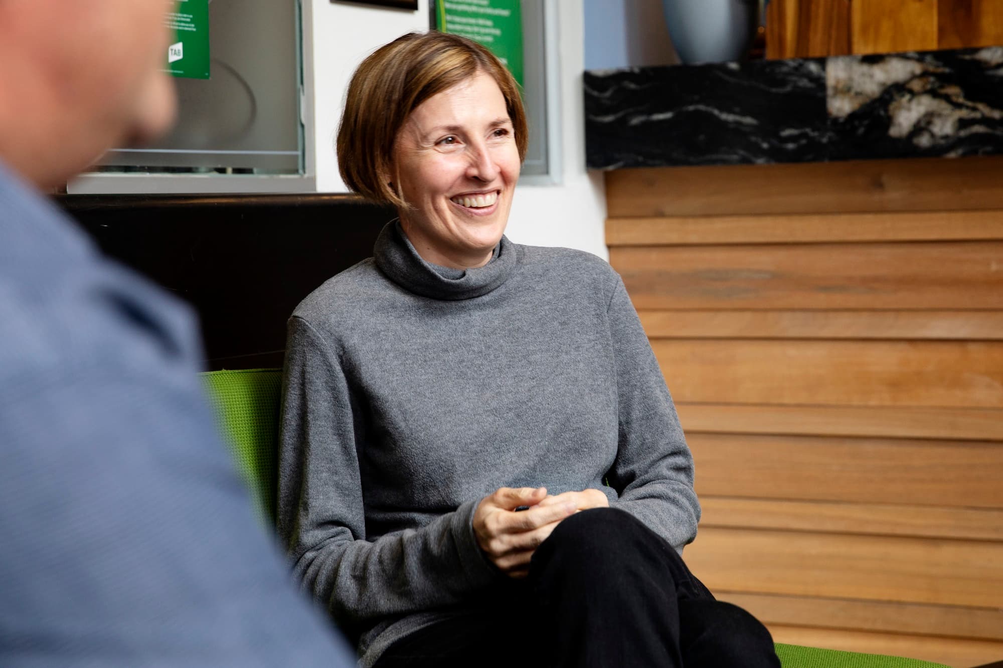 A woman seated in a chair participating in an MS Plus community support group.