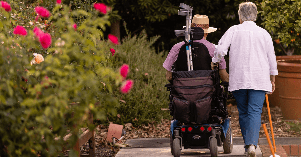 Rear views of a man using a wheelchair and a woman walking beside him.