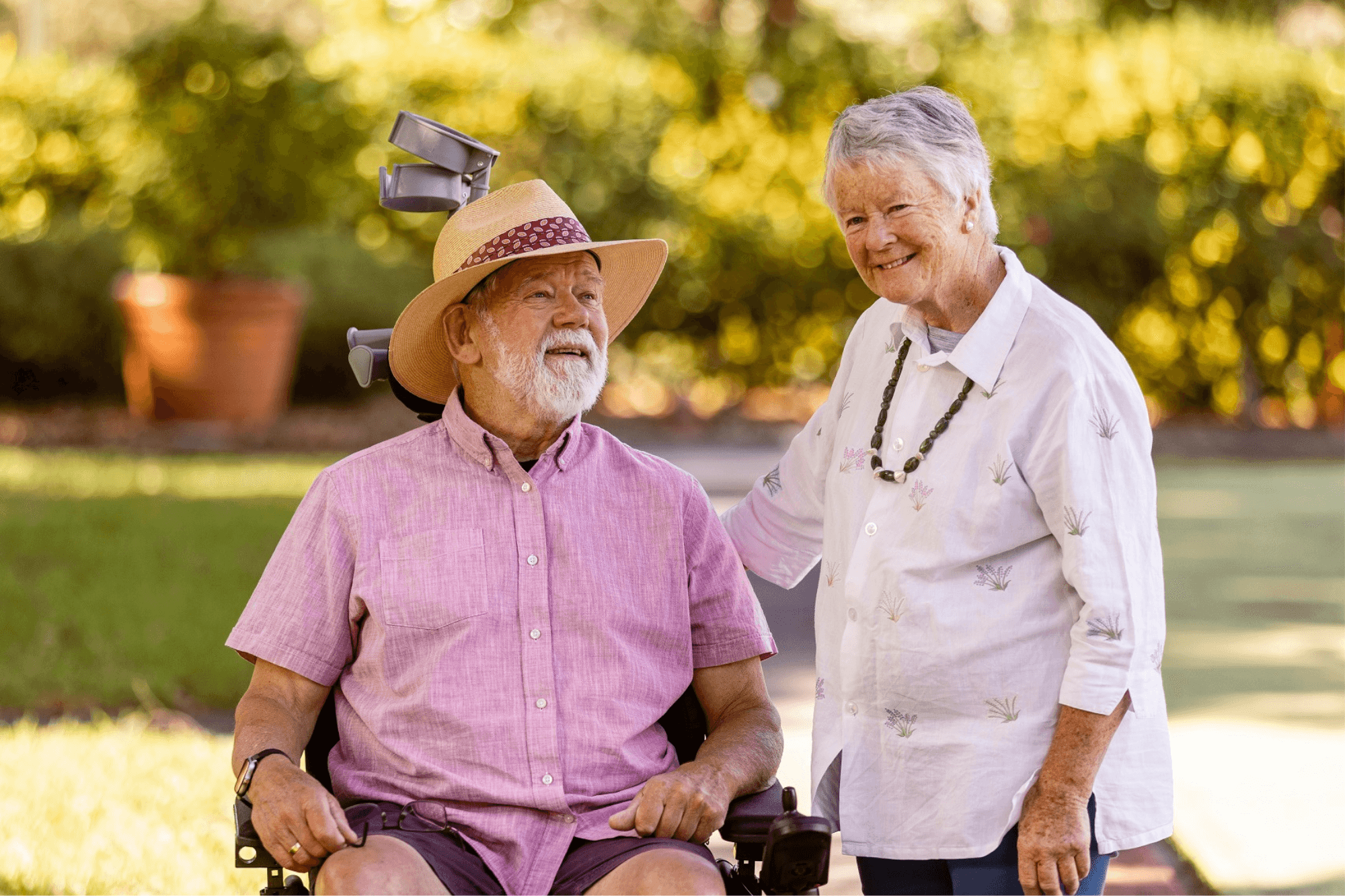 A man living with multiple sclerosis using a wheelchair with a woman standing beside him.