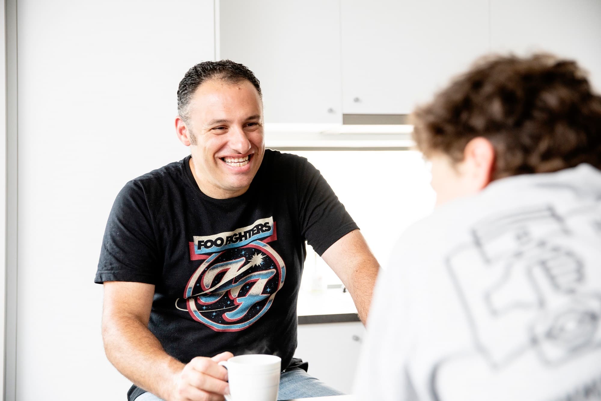 A man with a coffee mug smiling and speaking with another man