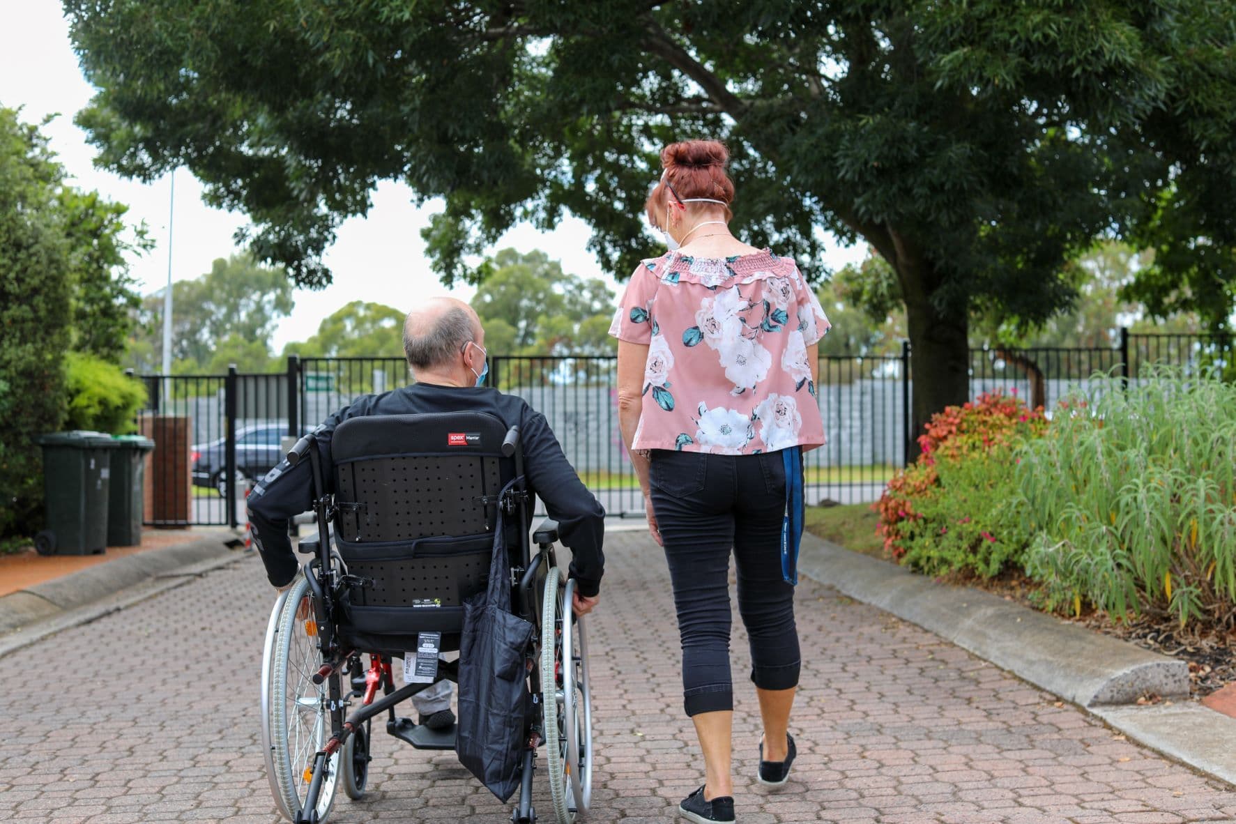 A rear view of a man using a wheelchair and a woman walking beside him.
