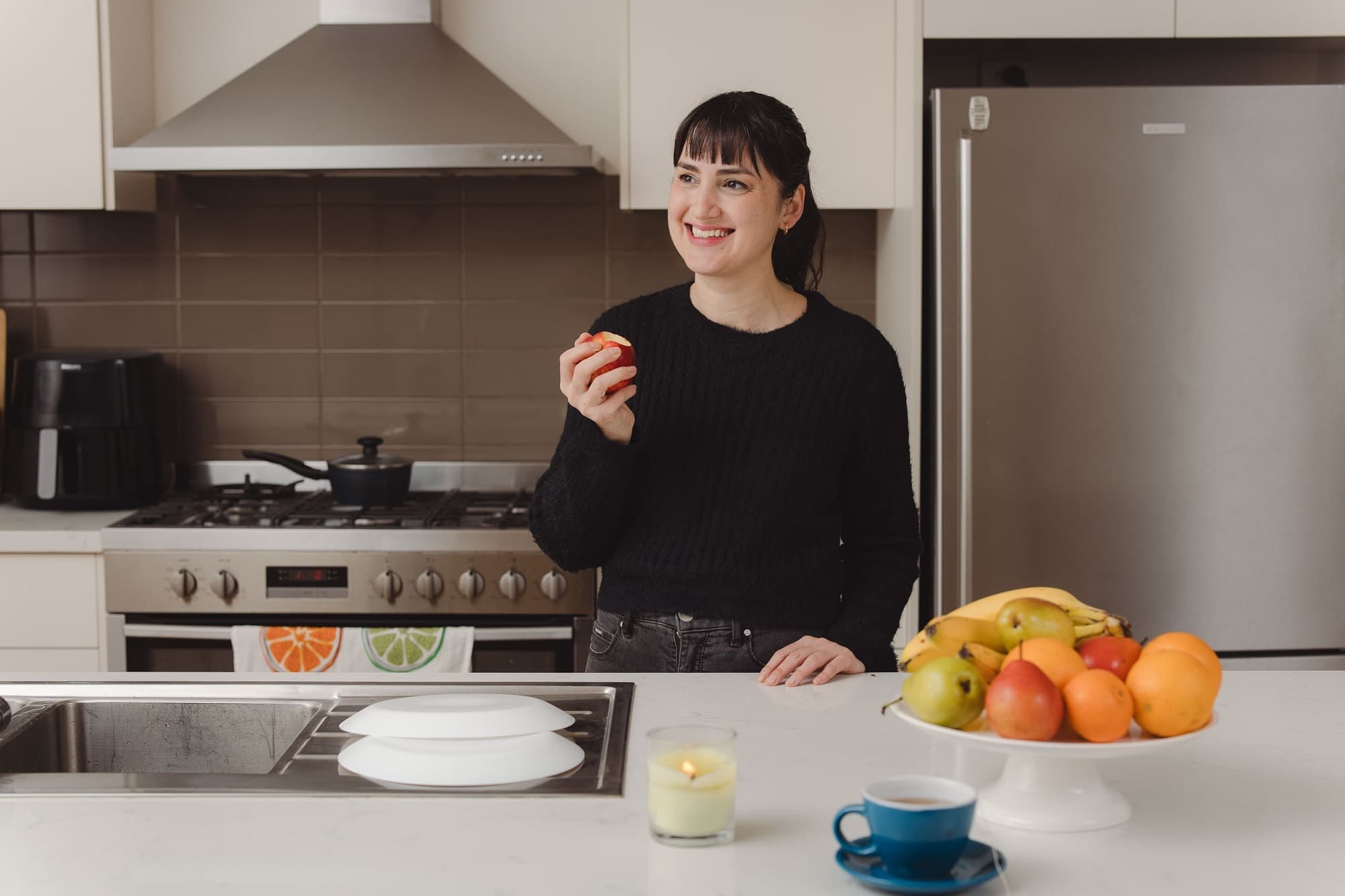 A lady wearing black shirt eating apple standing in kitchen
