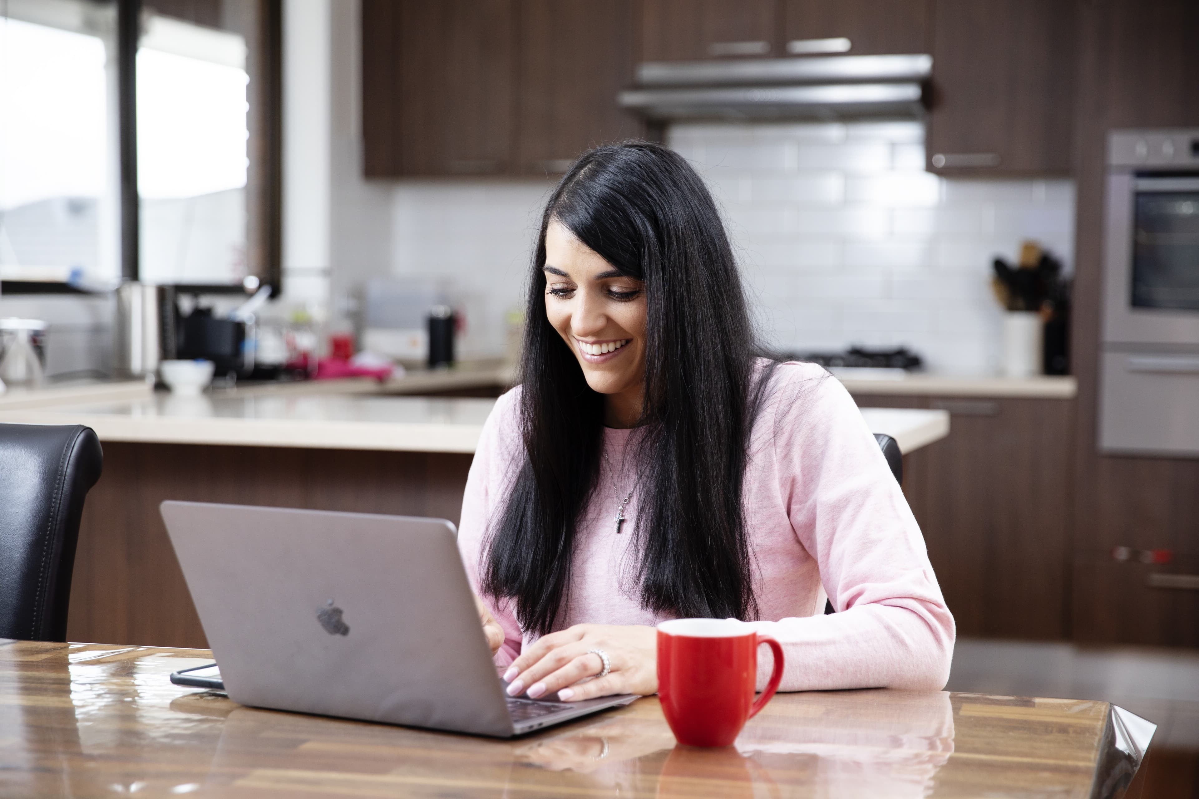 A woman seated at a kitchen table working on a laptop.