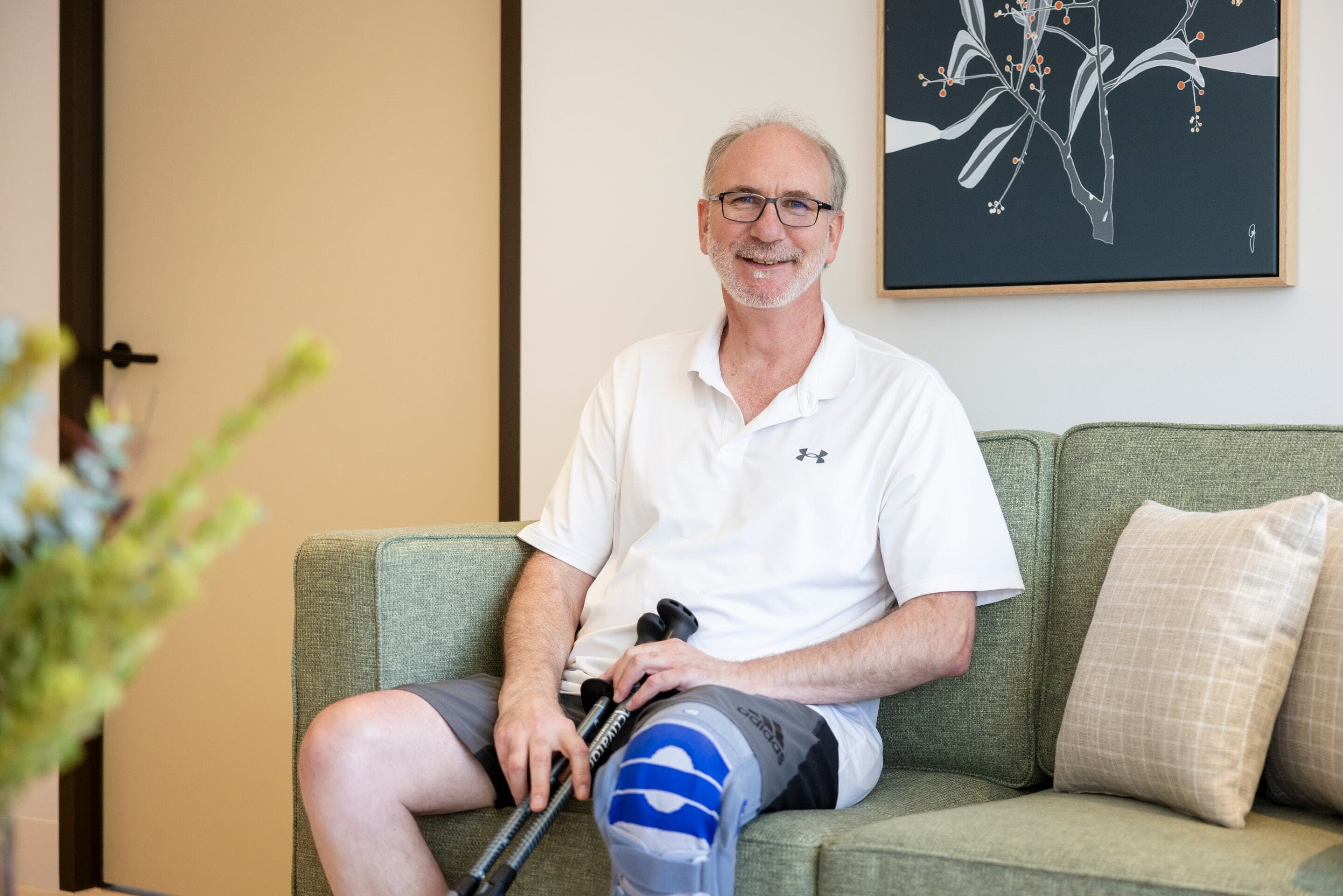 A man seated on a couch holding mobility aids in Lidcombe Home supported accommodation.