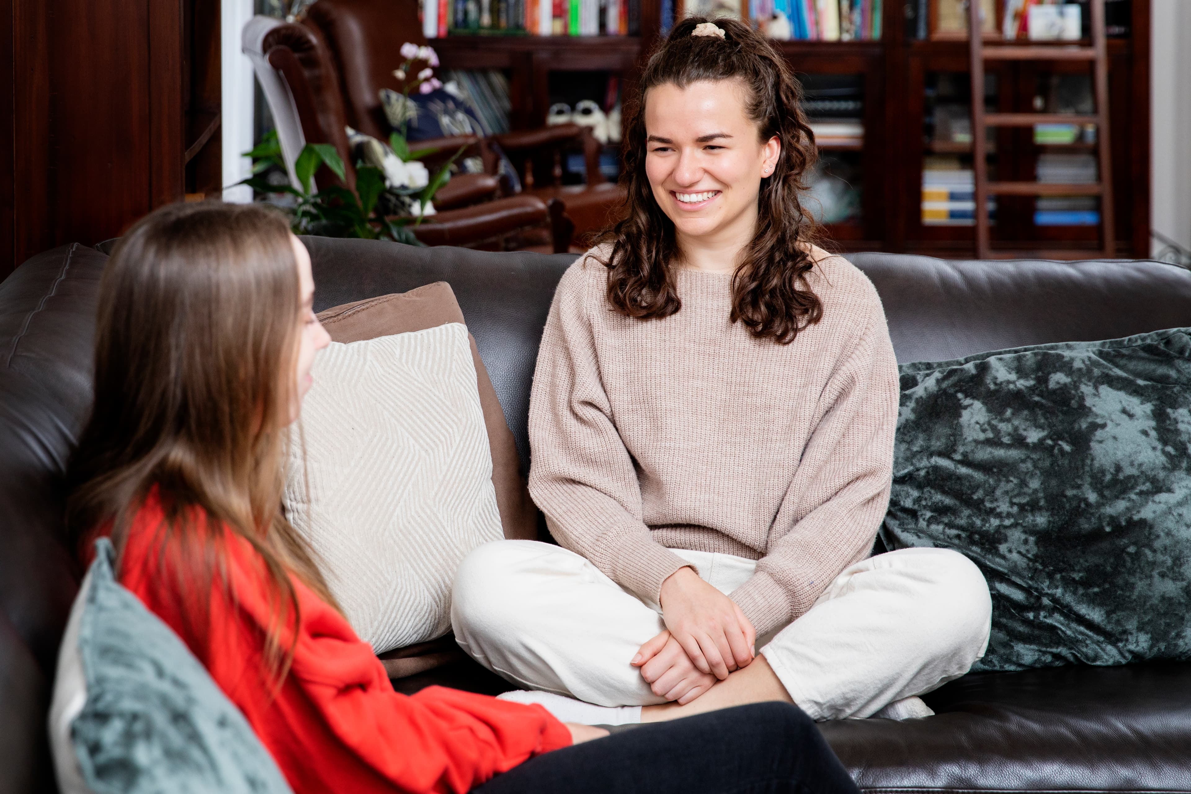 Two women seated on a couch facing each other, one providing support to the other who is living with multiple sclerosis.