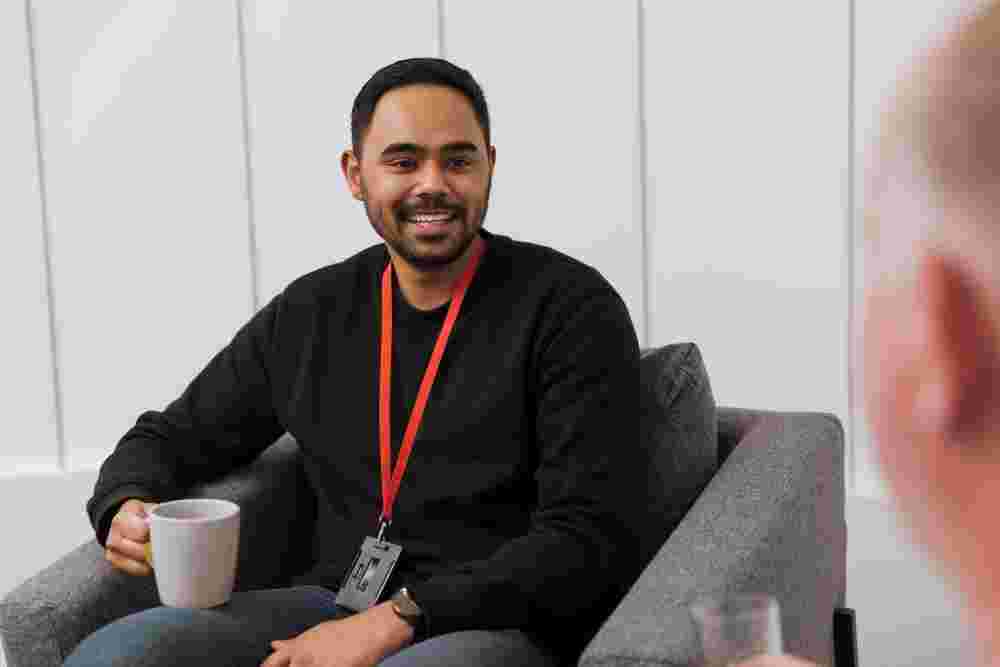 A staff member of MS Plus, seated in a chair, holding a beverage cup and talking to an MS Plus client.