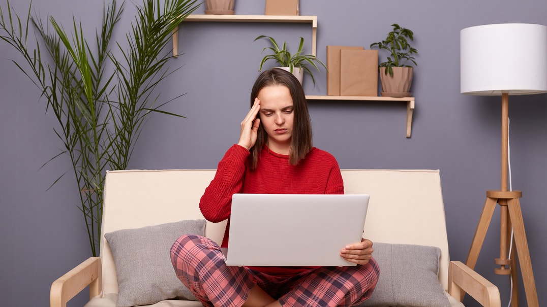 Person in pajamas with laptop holding head