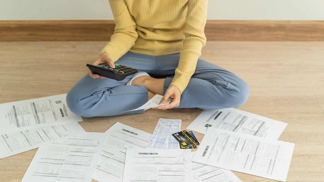 Person sits crosslegged on floor surrounded by paperwork