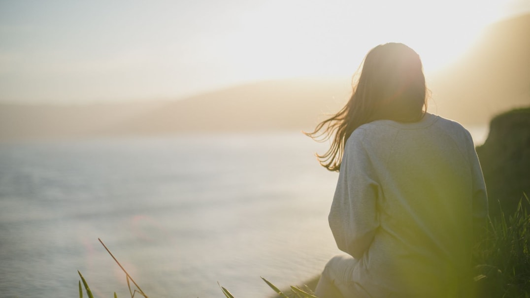 Person sitting on a cliff looking at the water