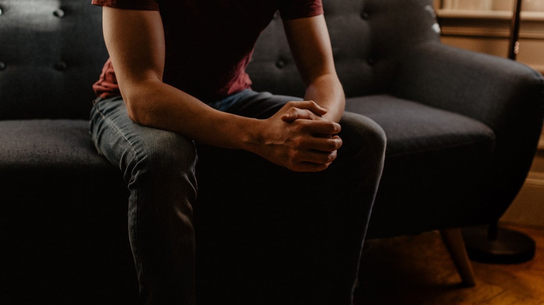 Person sitting on a couch with their hands clasped