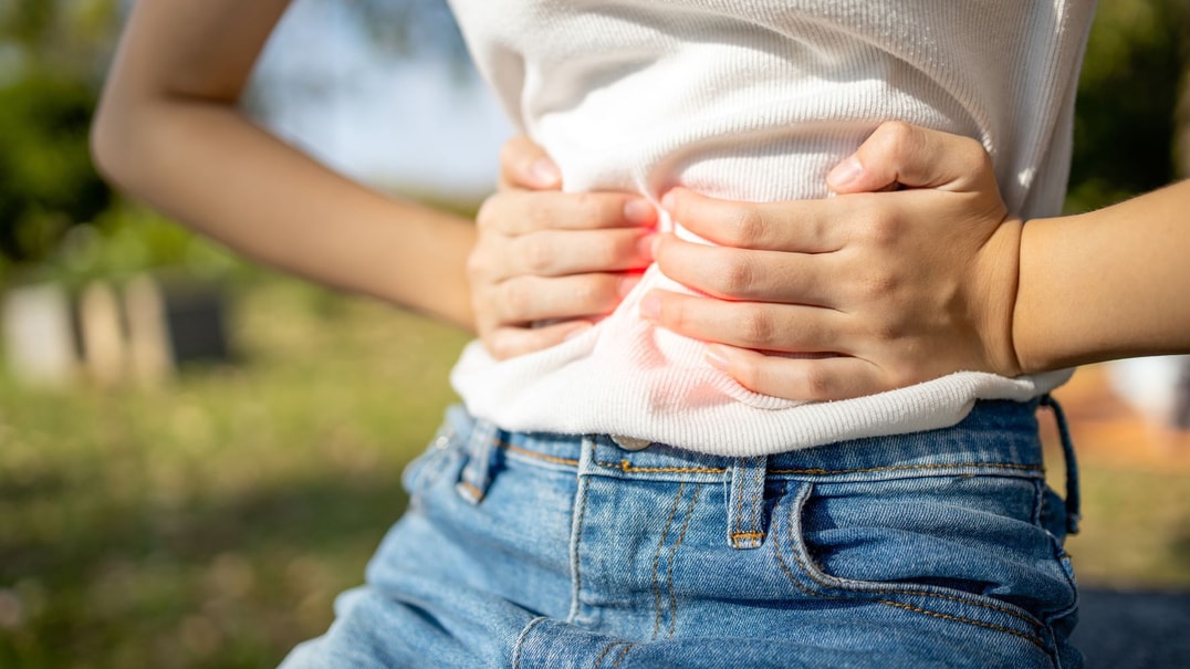 Person wearing jeans holds their abdomen