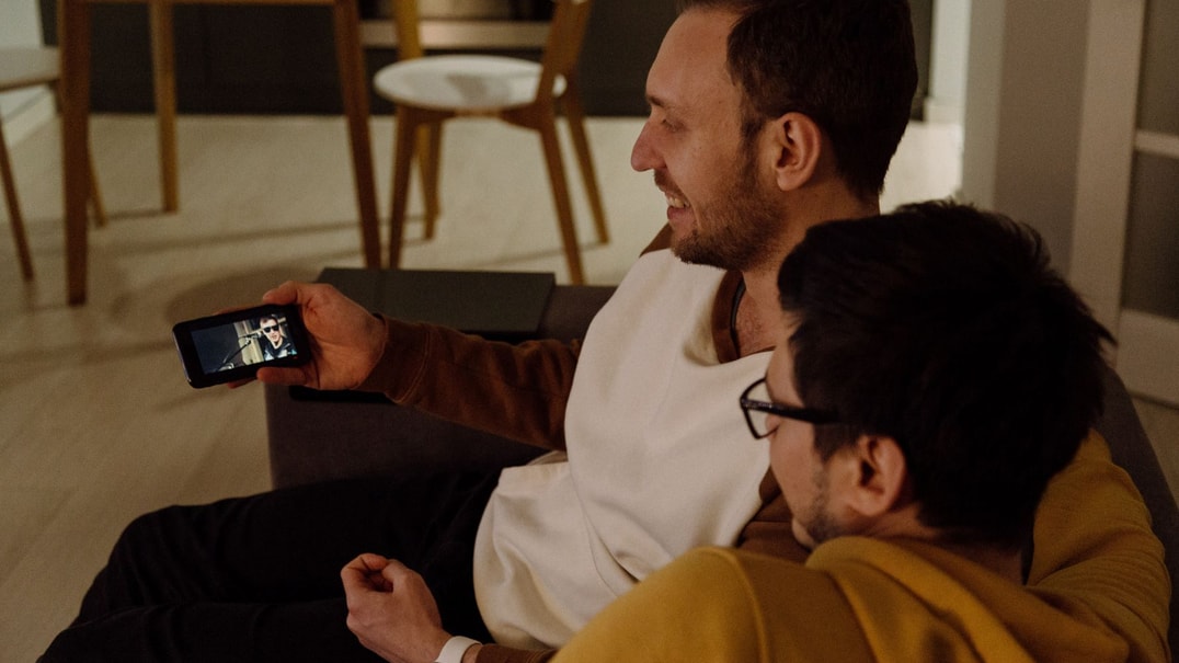 Two people are relaxing on a couch looking at an iphone