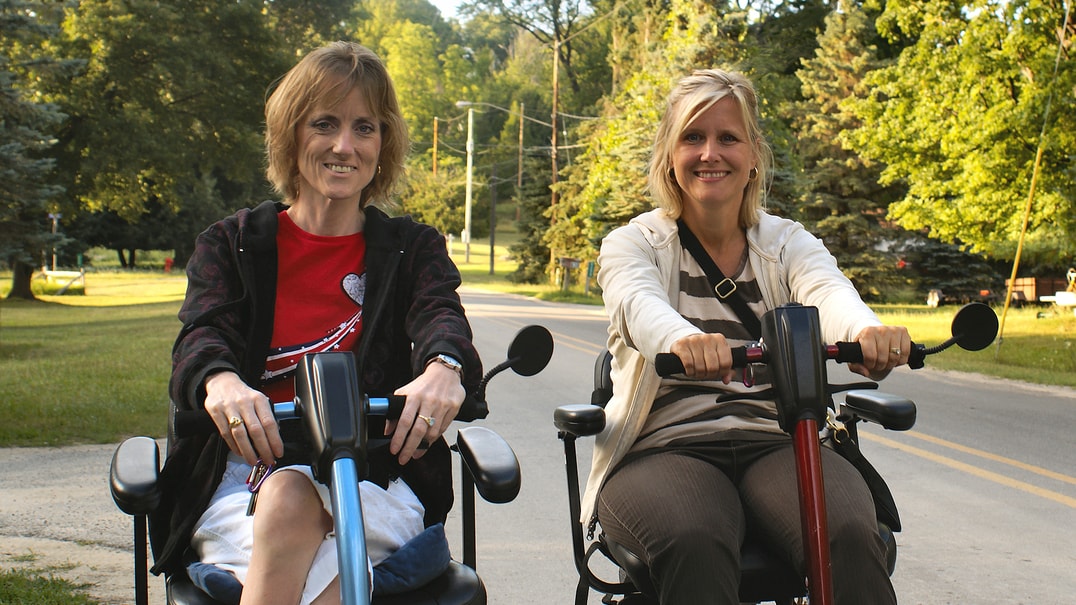 Two people riding mobility scooters outside