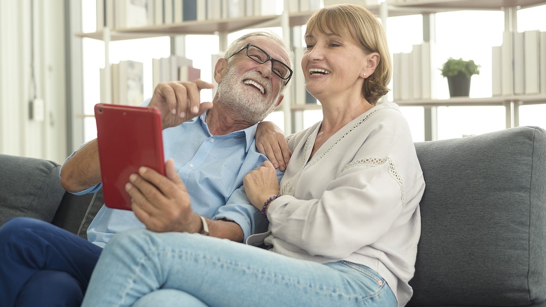 happy older people sitting on couch looking at ipod